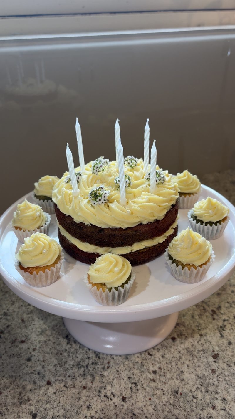 A naked layer cake with birthday candles, surrounded by matching mini cupcakes on a cake stand