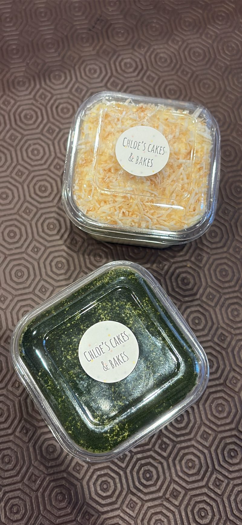 Individual mini cakes, one topped with toasted coconut and one with pandan, each packaged individually