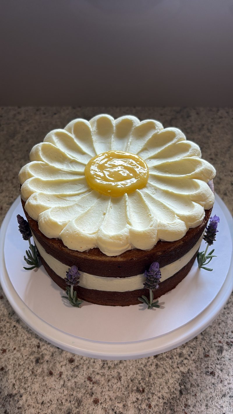 A naked layer cake with a piped daisy design, lemon curd centre and fresh lavender sprigs